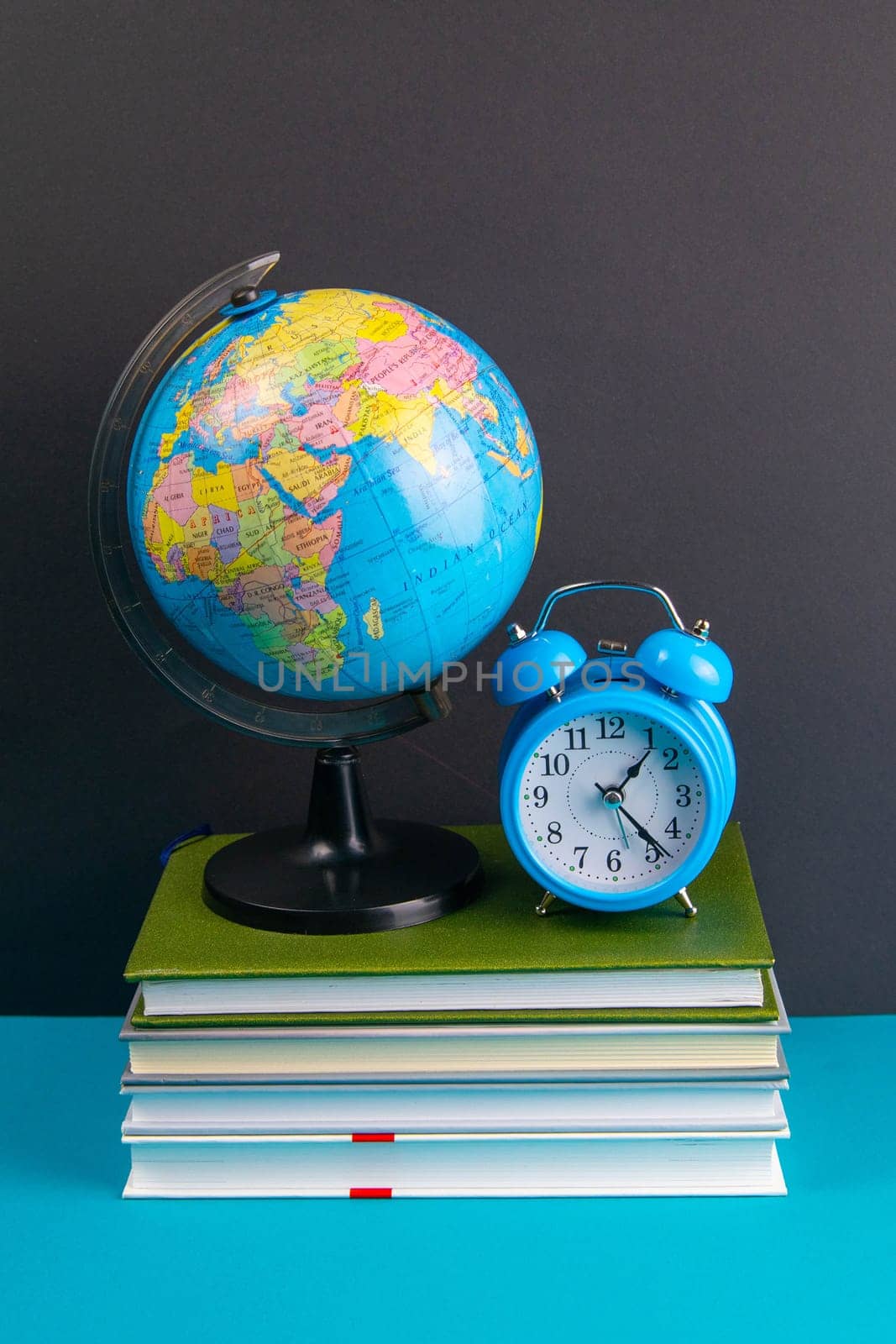 The globe and clock stand on a stack of books, on a blue table.