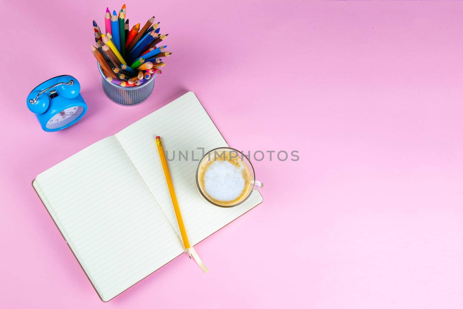 Pencils, note book and clock on the pink table. business conceptual. Top views with clear space