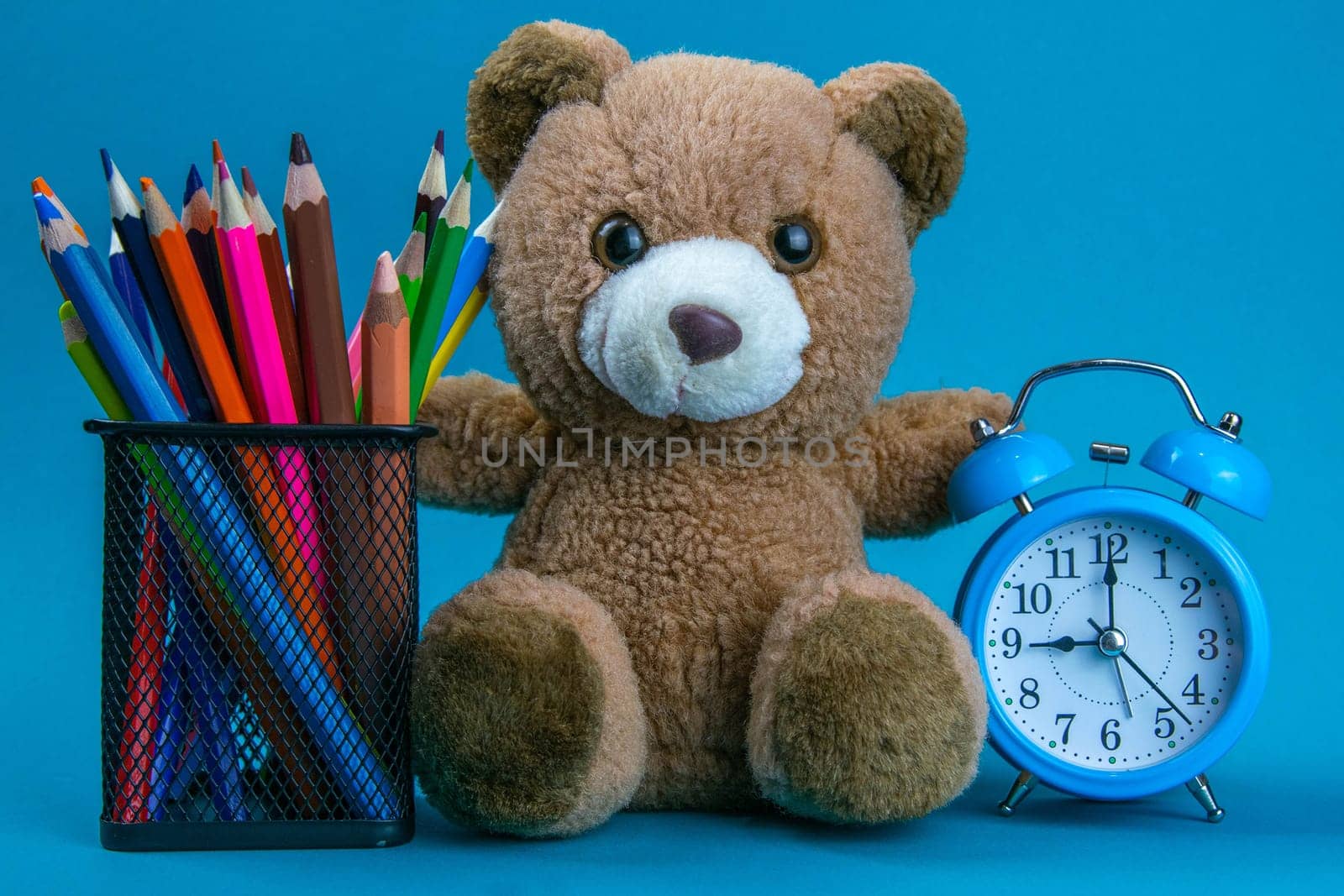 Blue alarm clock with brown bear and colorful pencil placed on the wooden table. Time to work. Use for background and texture.