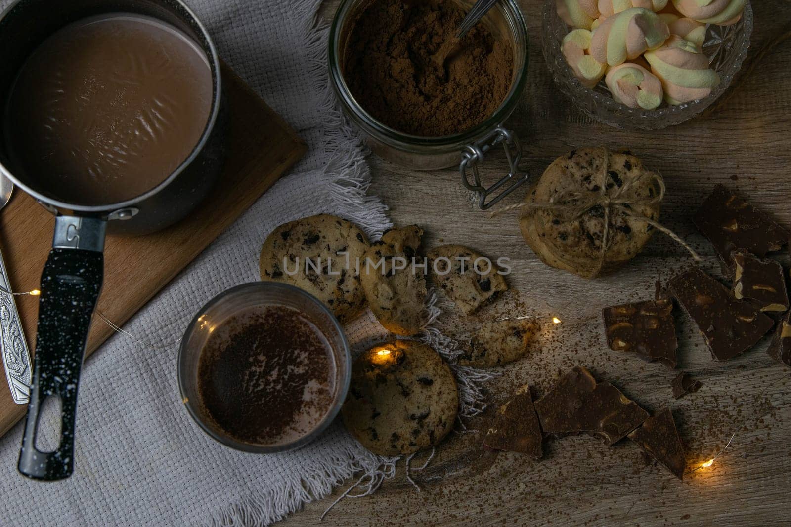 Cocoa with marshmallows and chocolate oven and slices of chocolate stands on a wooden table.