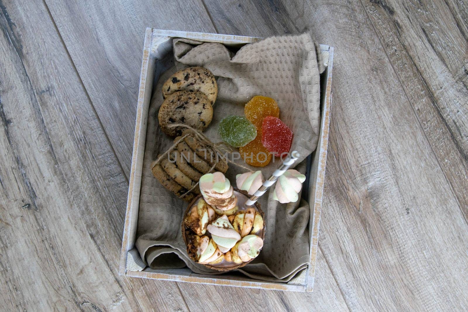 Cocoa with marshmallows and chocolate baking and slices of chocolate and jelly candies stand in wooden box on wooden table.
