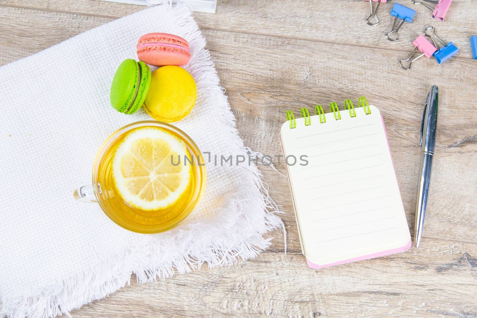 An open notebook with a silver pen, a cup of mint tea with lemon and multi-colored muffins stand next to it.