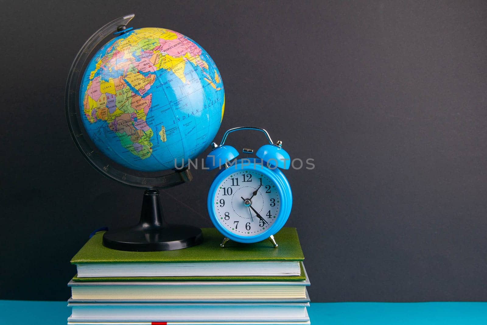 The globe and clock stand on a stack of books, on a blue table.