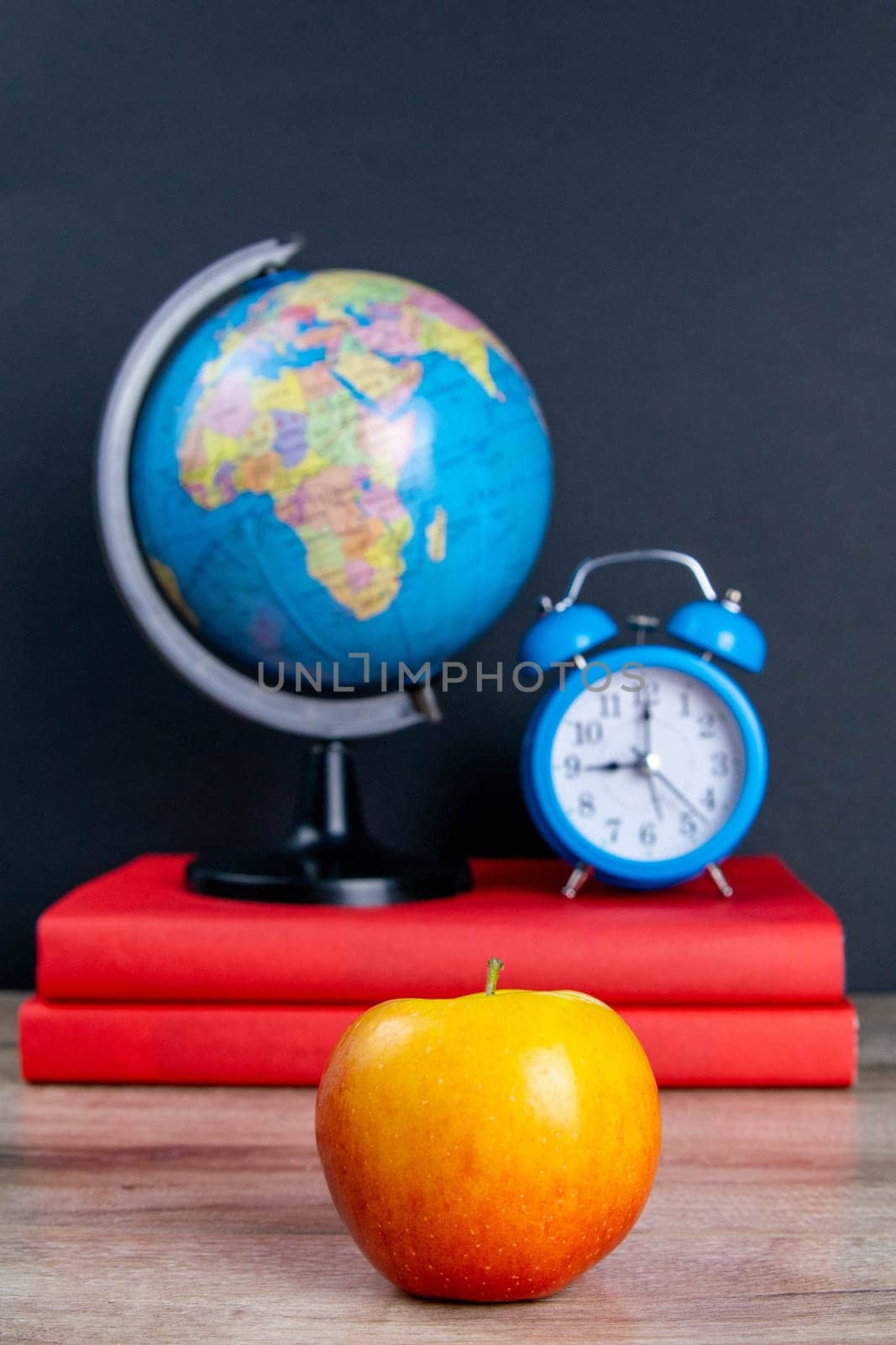 The globe and the blue clock stand on a stack of books, next to an apple.