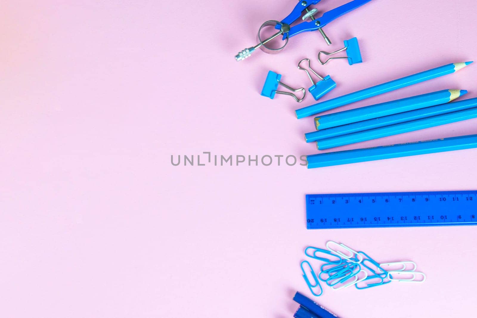 Multi-colored blue pencils rulers, pens, pencils and scissors and stationery stand on a pink background.