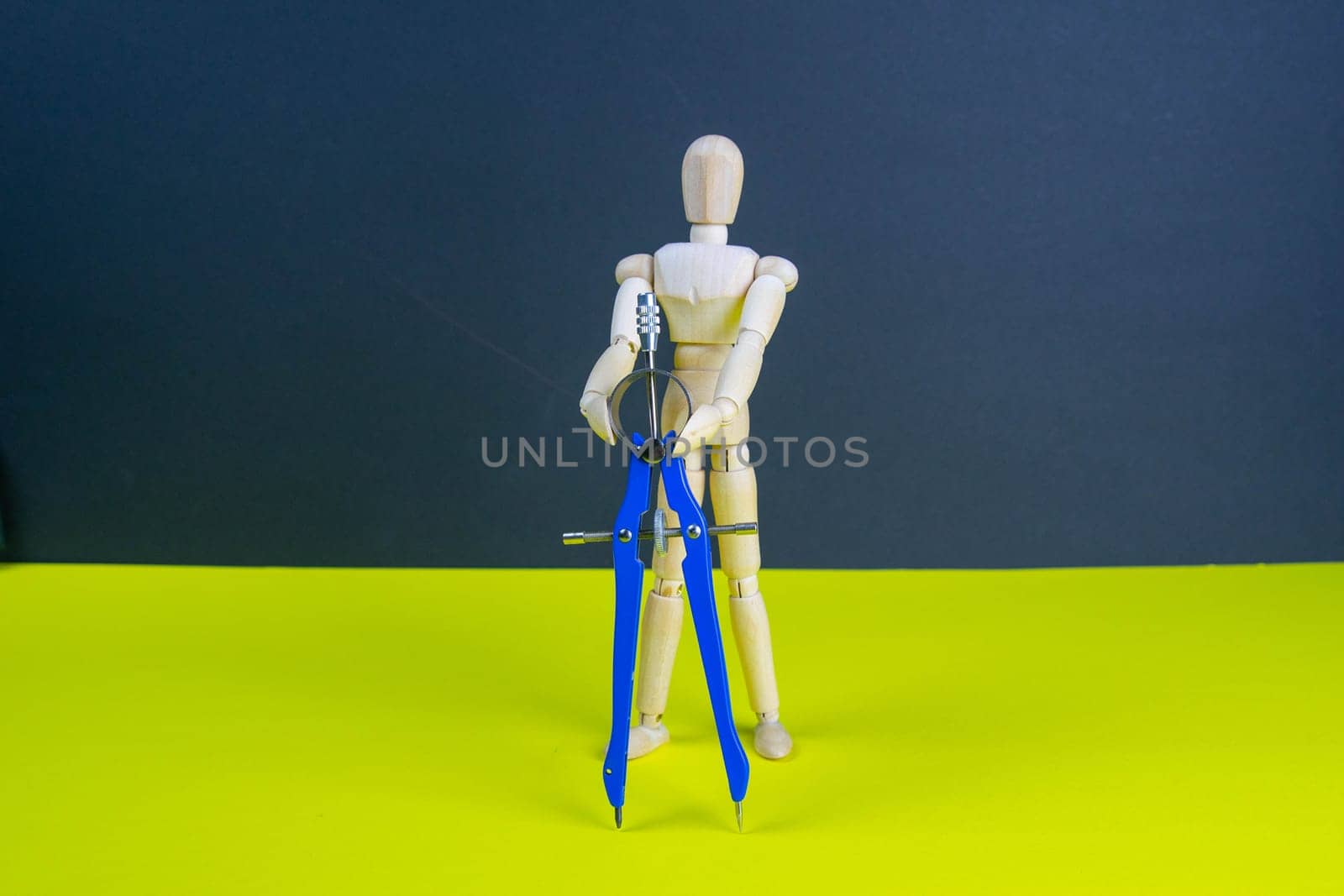 Wooden man figurine with compass on the yellow table.