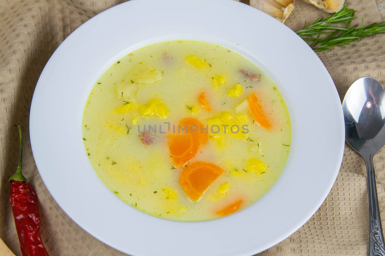 Potato cream soup with mushrooms, carrots and cheese. Top view. The plate is on a coffee towel, there is a spoon next to it.