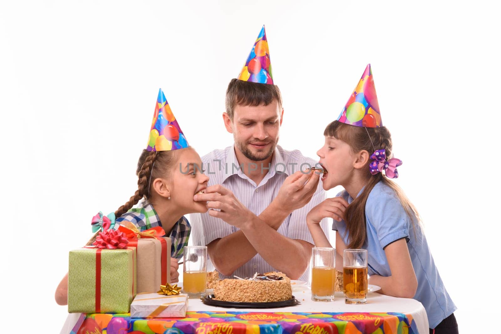 Kids bite pieces of cake from dad's hands, having fun celebrating a birthday