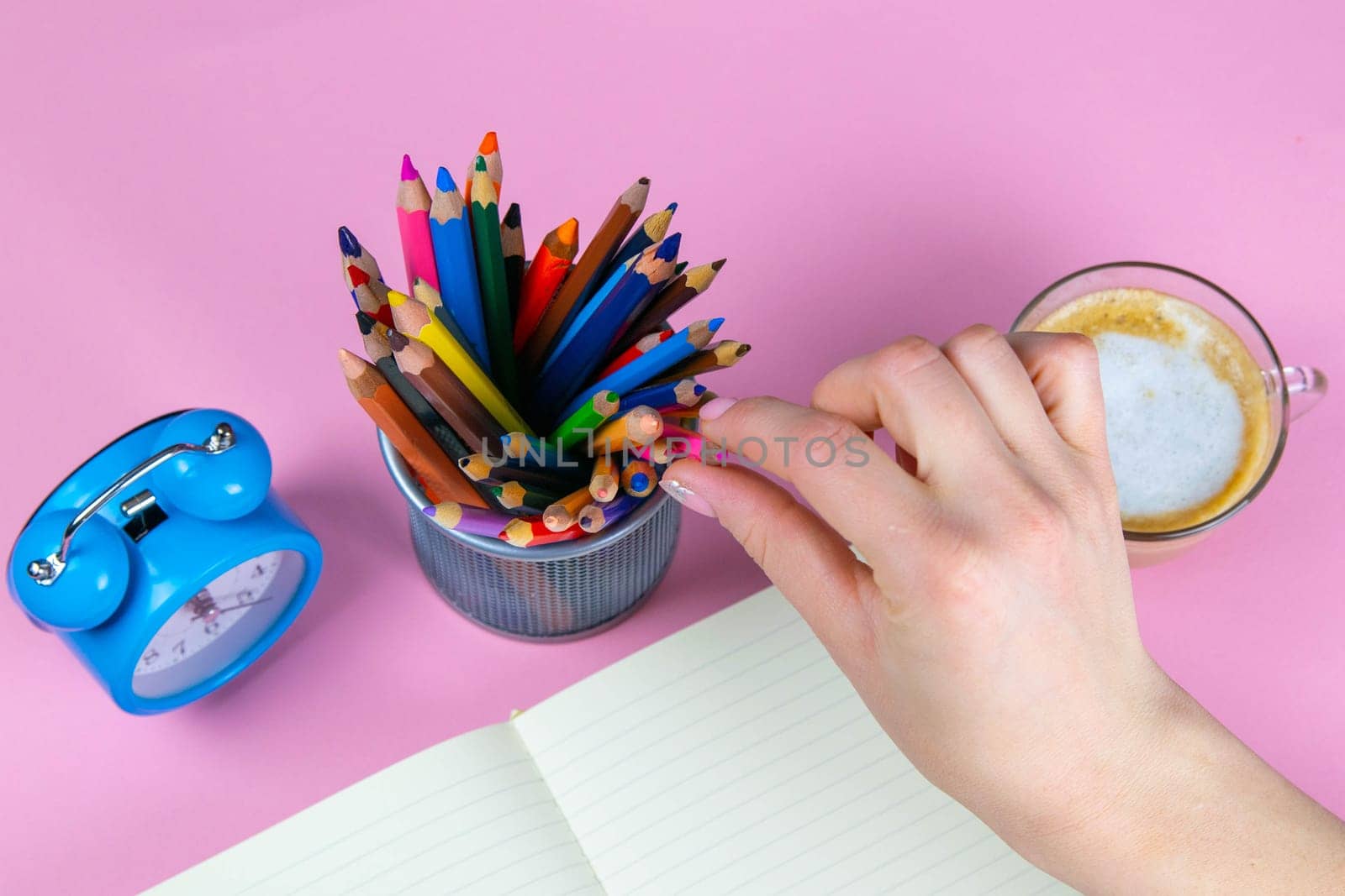 Tablet with white Leaf, next to which is a green plant, a glass with pencils. Hand holds a pen and writes a clock on the sheet in another hand.