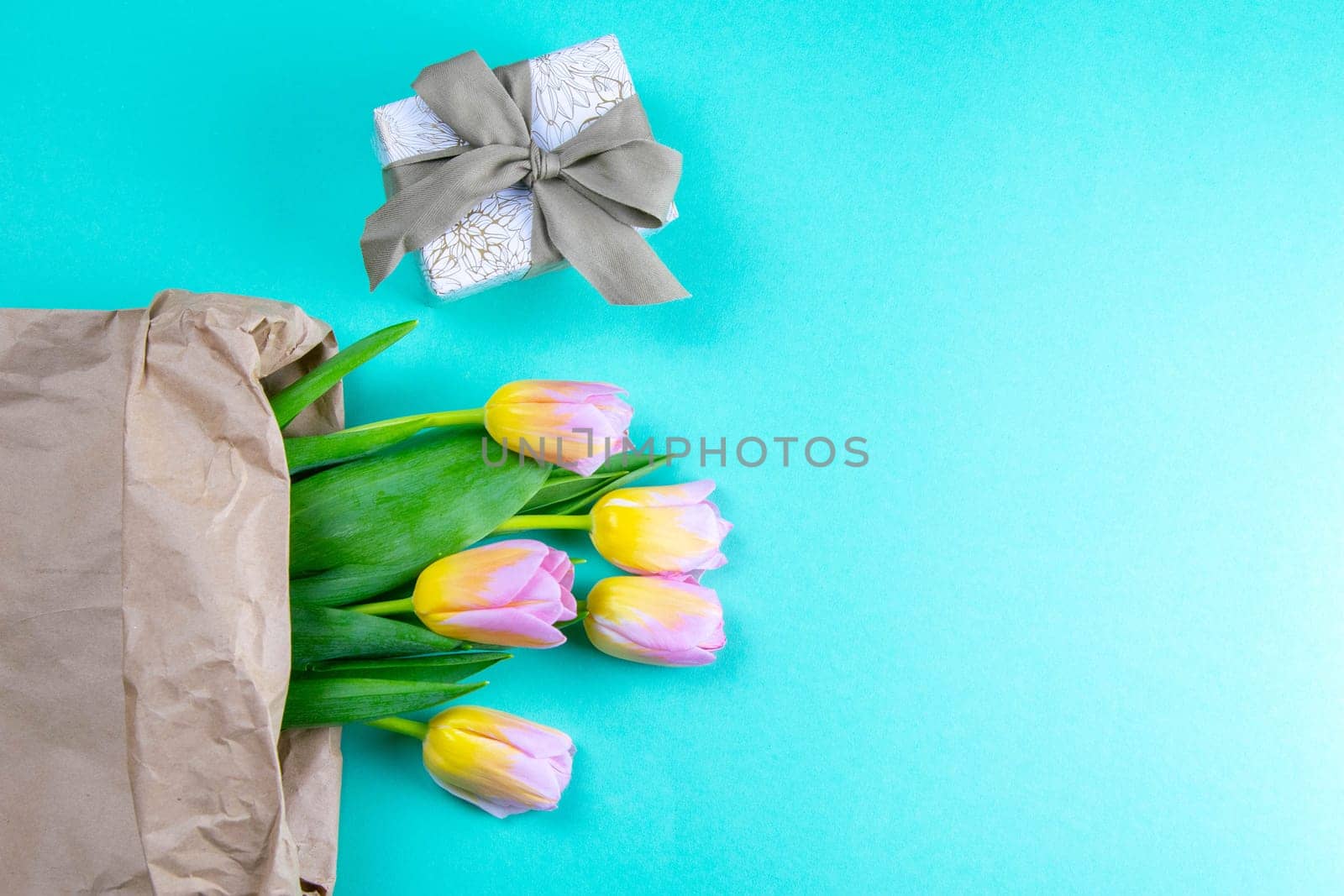 Bouquet of yellow tulip flowers in brown paper bag with gift on mint background.