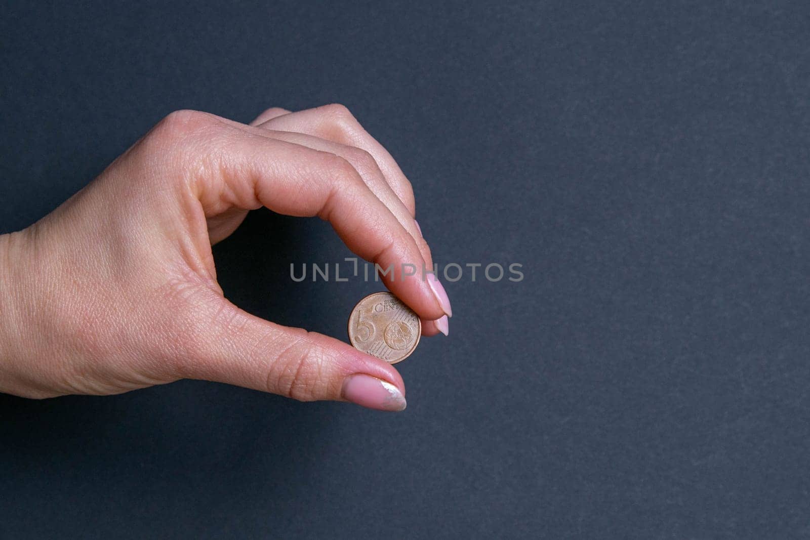 Hand sign by holding a coin, isolated on black background.