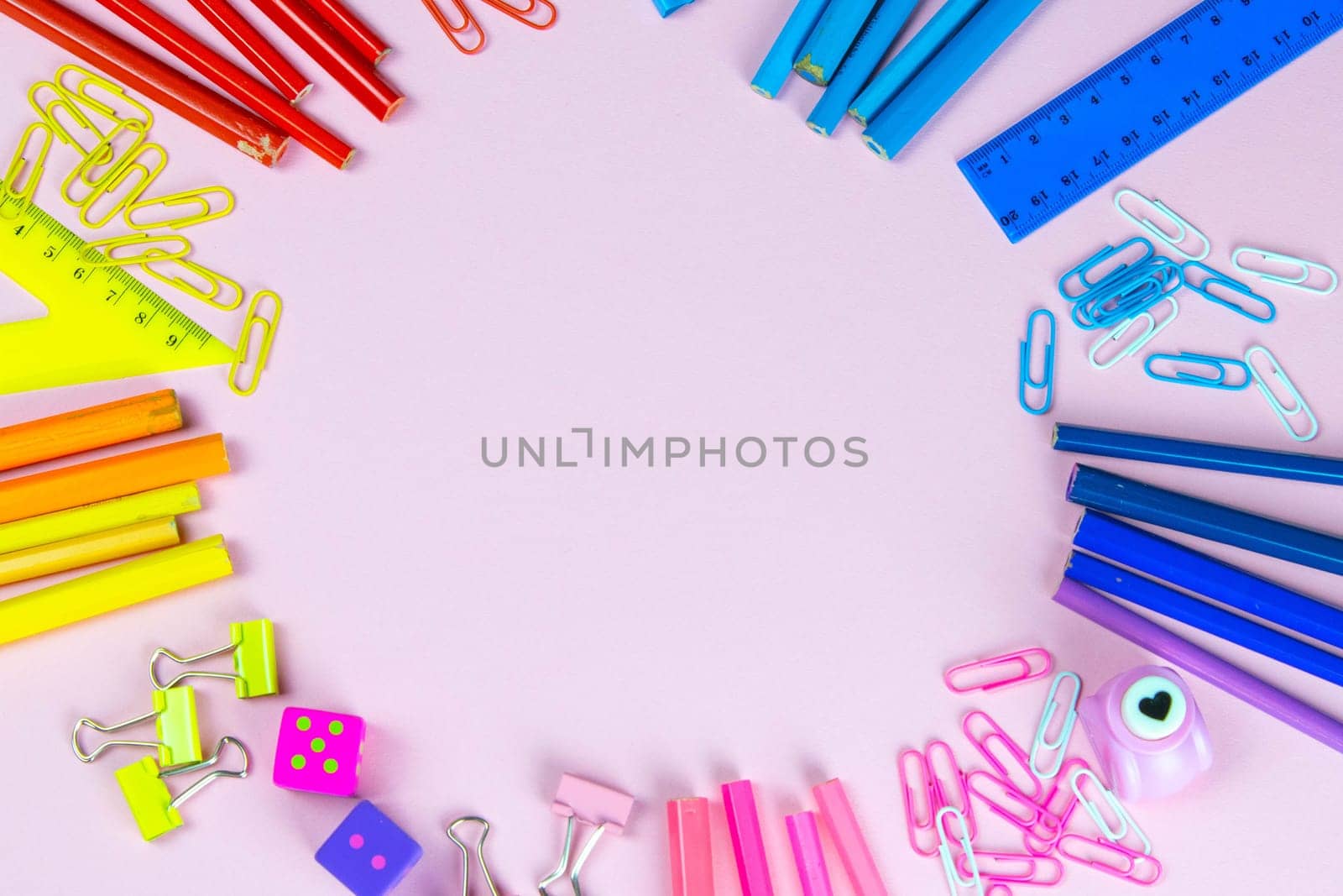 Multi-colored pencils rulers, pens, pencils and scissors and stationery stand on a pink background.