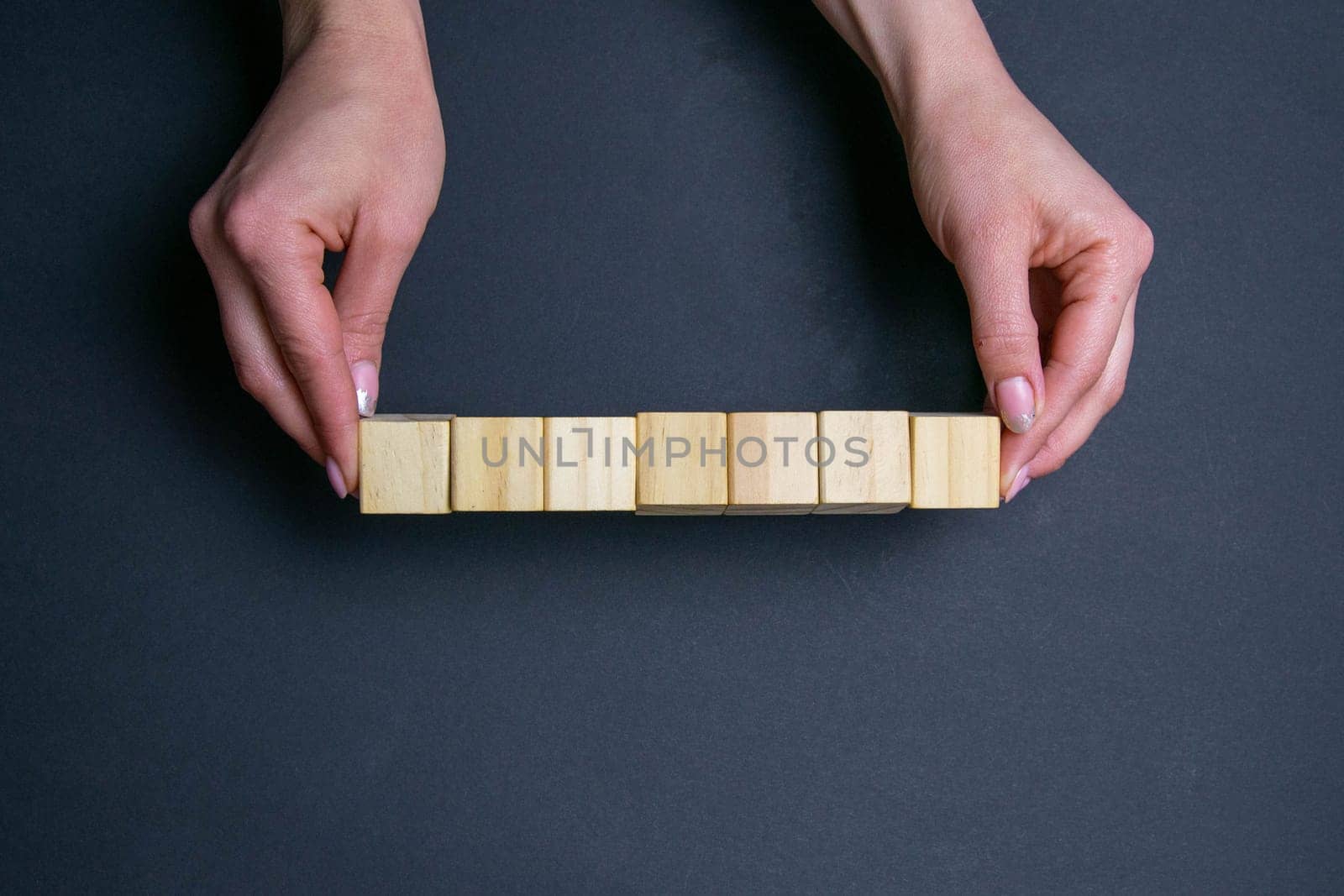 Two hands hold 7 wooden cubes, provided space for text.