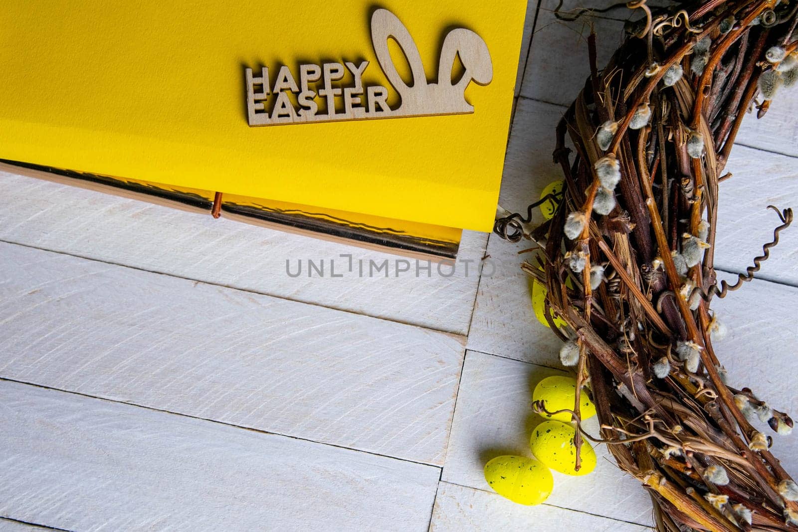 Easter concept. Yellow notepad with a sign of the sorly Easter and a wreath stand on a white wooden table.