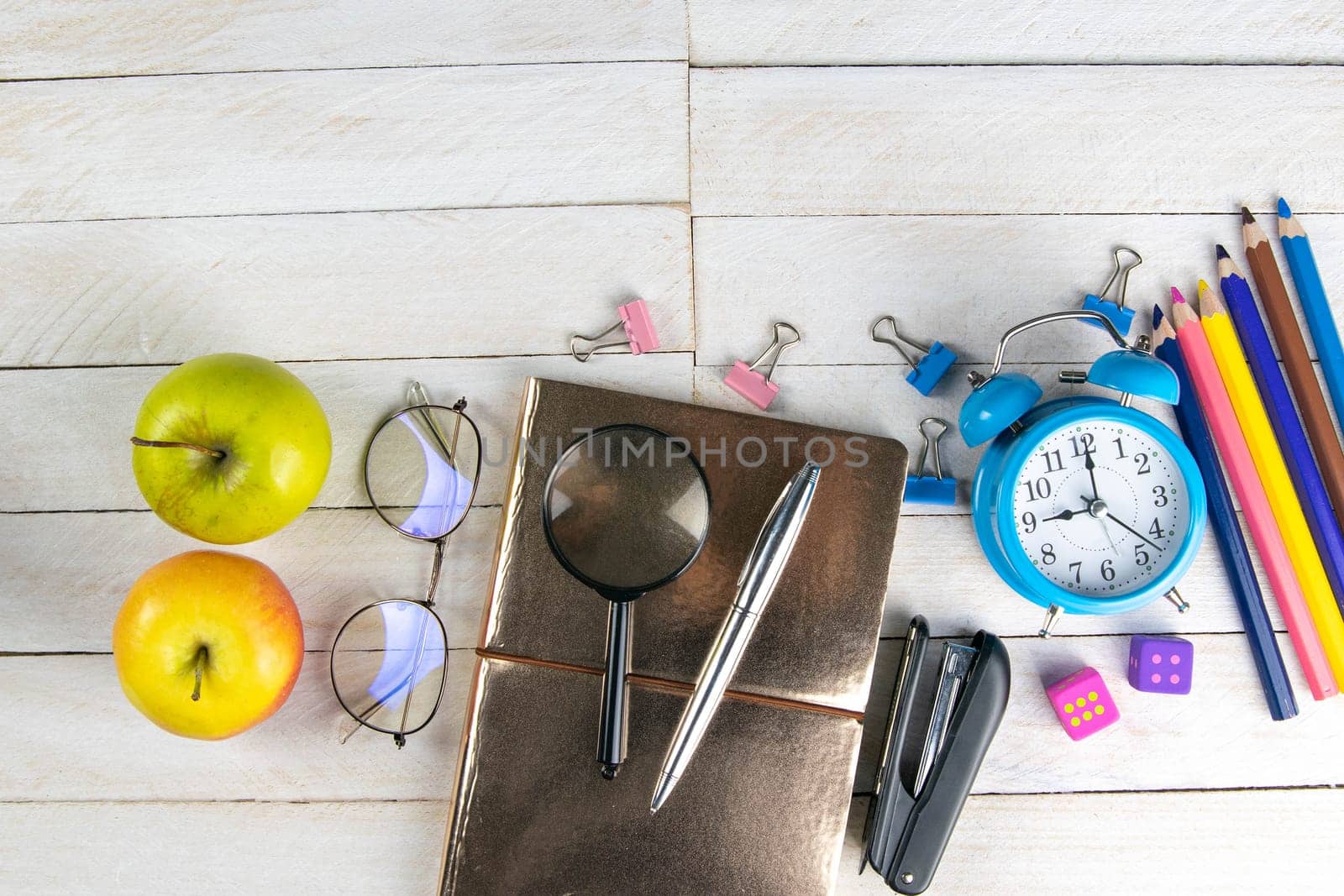 Various office stationery, notepad, clock, pencils, ooh, glasses, pen and two fresh apples on a white wooden table. Top view with copy space. Concept of office, education, workplace, school.