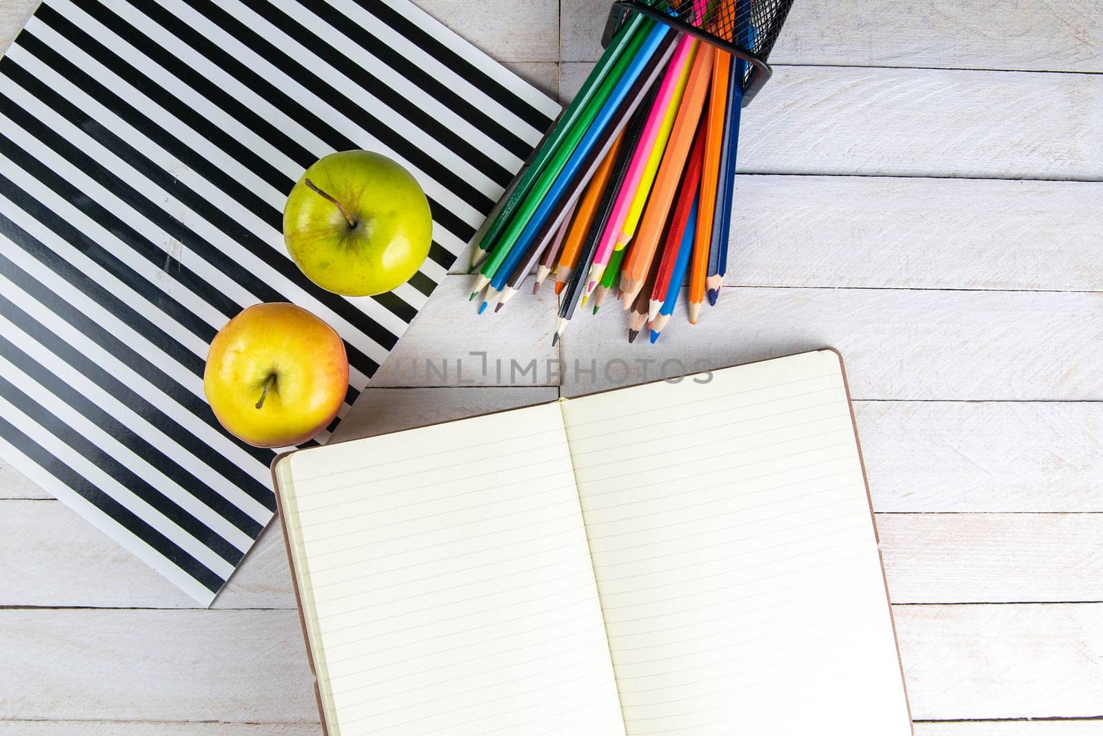 Top view of open notebook with empty pages, pencil and red apples on wooden table in office workspace.