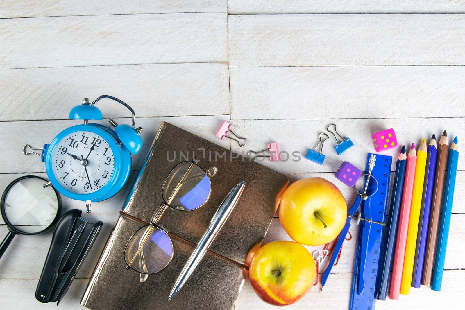 Various office stationery, notepad, clock, pencils, ooh, glasses, pen and two fresh apples on a white wooden table. Top view with copy space. Concept of office, education, workplace, school.