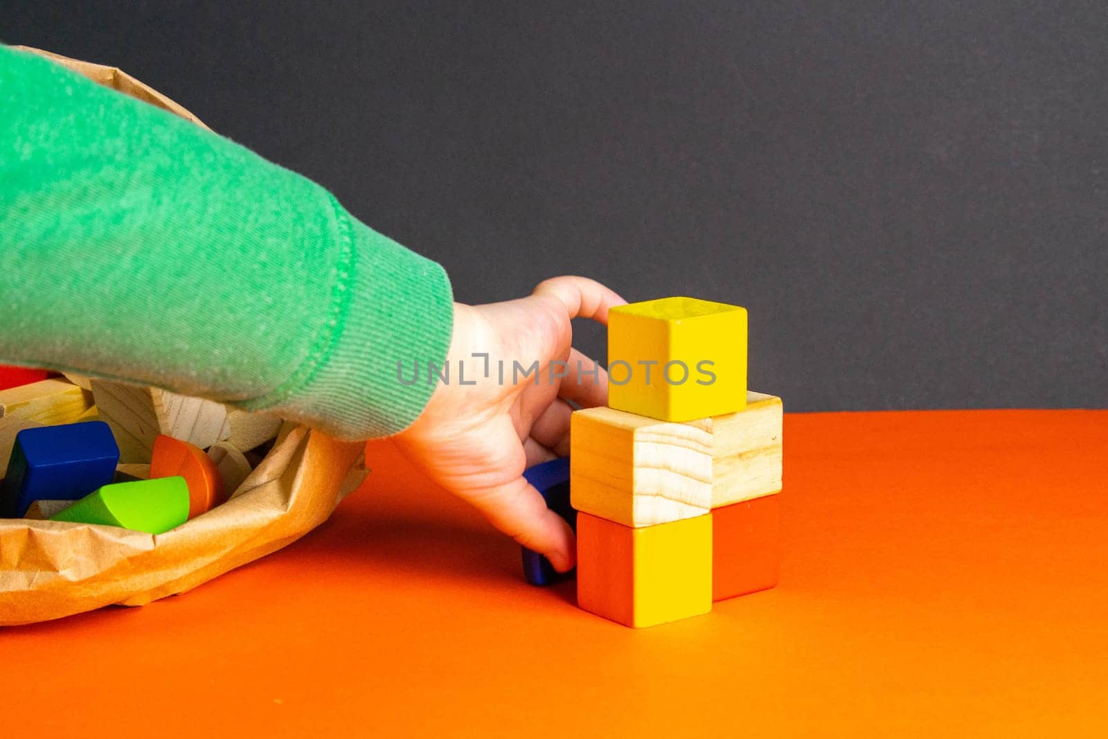 A child plays with wood cubes on an orange background.