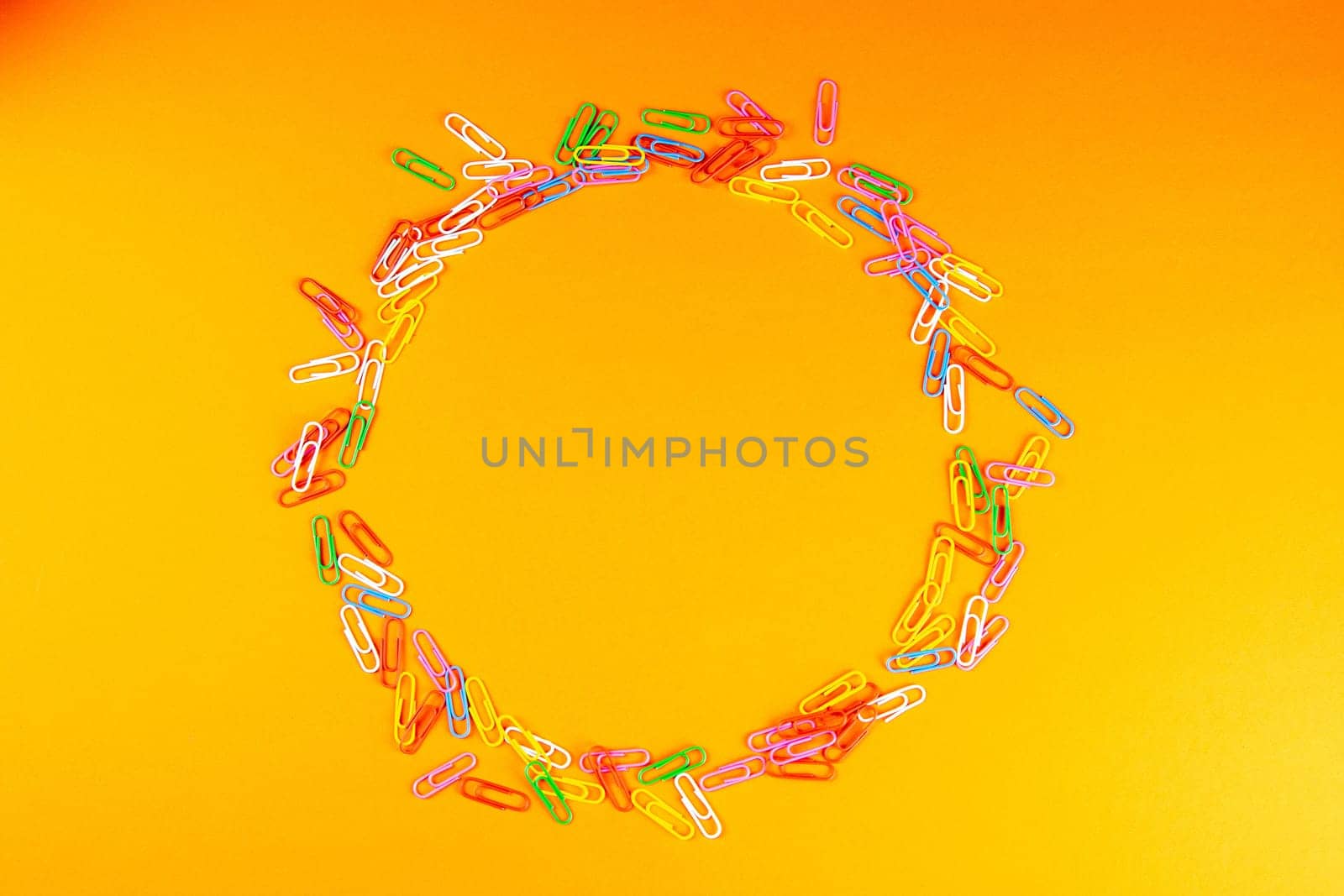 Pile of colored paper clips arranged in a circle on an orange surface.
