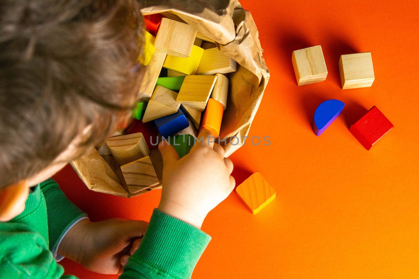 A child plays with wood cubes on an orange background.