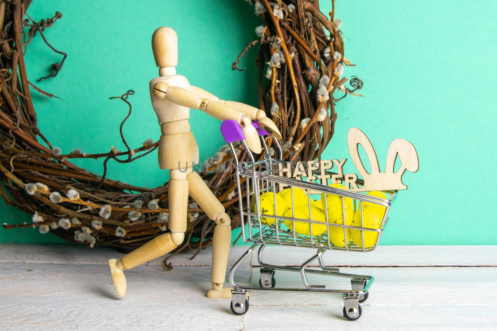 The Easter concept. Figure of a wooden man with a basket filled with eggs. In the background is a wooden rabbit and a sign of a Happy Easter and a wreath.