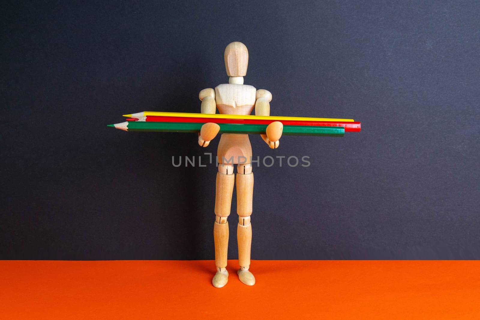 The figure of a wooden man holds pencils of different colors.