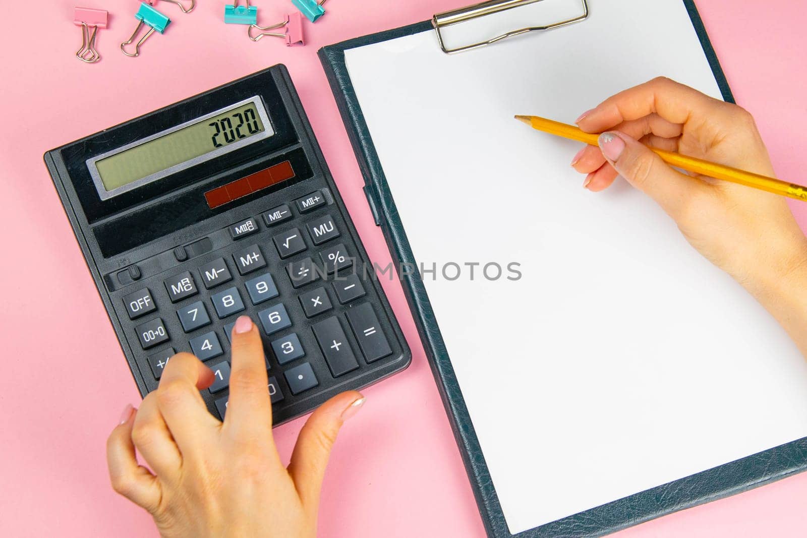 The hands of a woman count on a calculator and write notes. Top view of business woman's hands on white sheet. Finance and business concept.