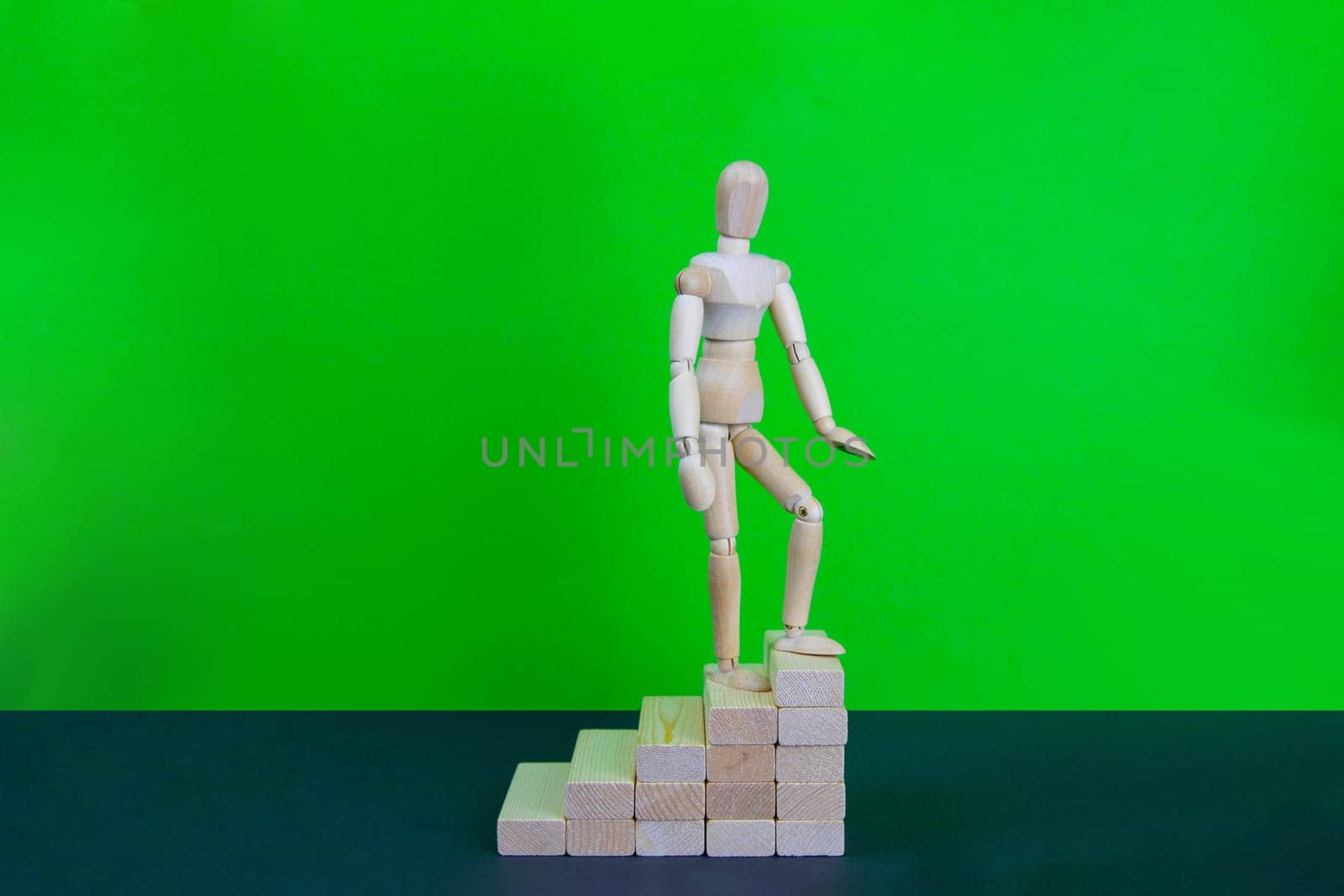 Wooden man walk up the career stairs. Ladder made with wooden bricks. Mannequin on top of development. Concept of personal development, career , changes, success. Green background, copy space for ad.