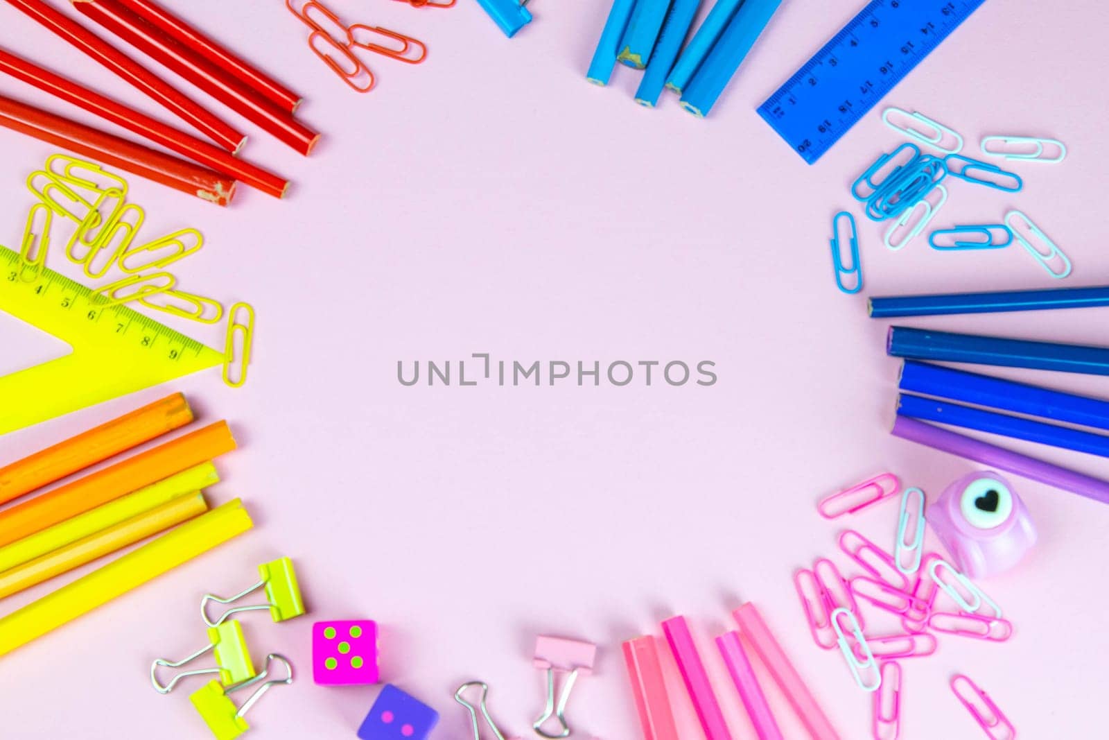 Multi-colored pencils rulers, pens, pencils and scissors and stationery stand on a pink background.