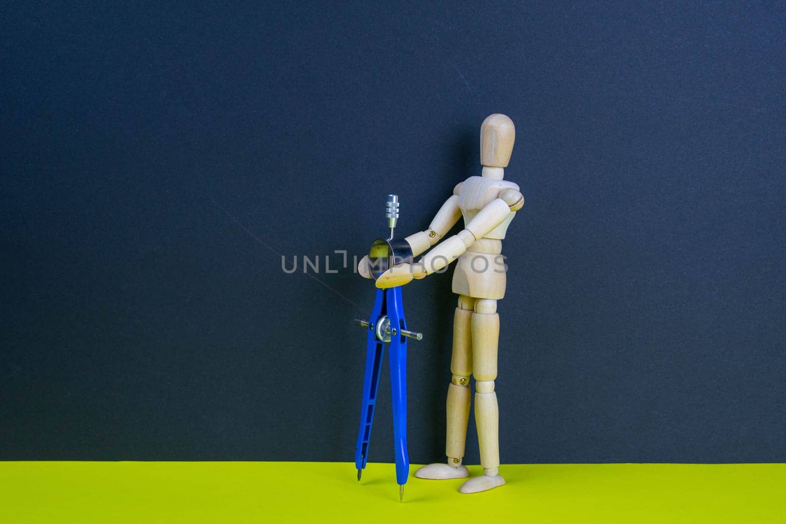 Wooden man figurine with compass on the yellow table.