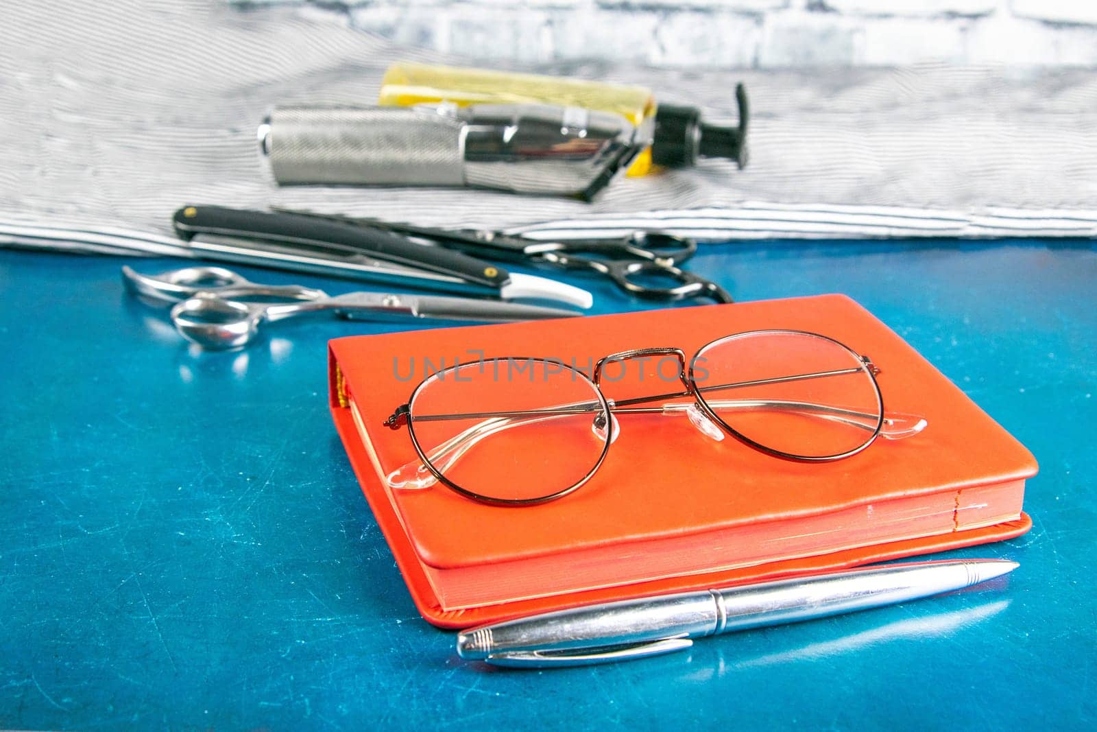 Hairdressing tools set, Red notepad with glasses and scissors, hair clipper, comb, dangerous razor, hair gel stand on blue background.