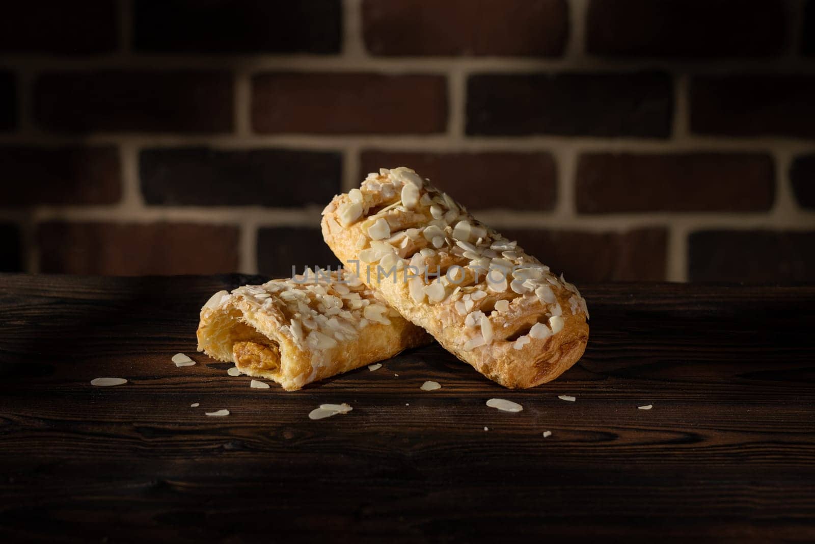 Caramel strudel with almond flakes on wood table and brick wall background