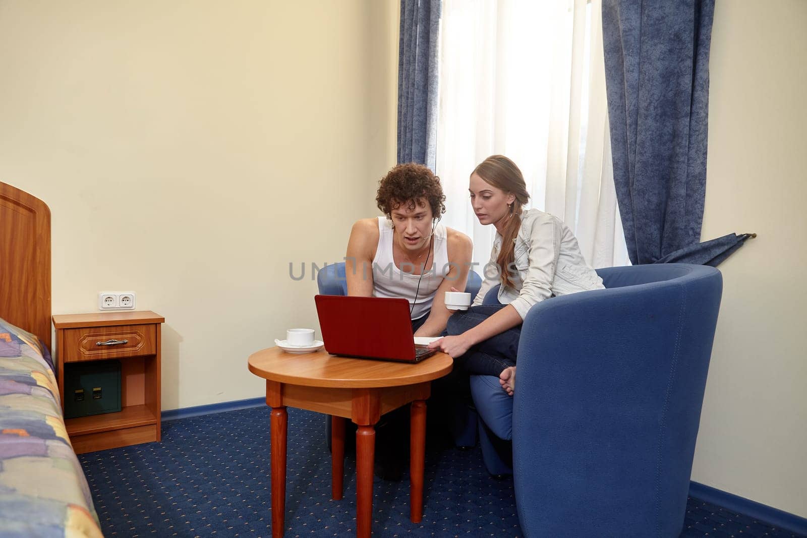 Happy young couple with laptop are sitting in armchair in living room at home. Internet communication. communication on network. Isolation period, quarantine, social distancing