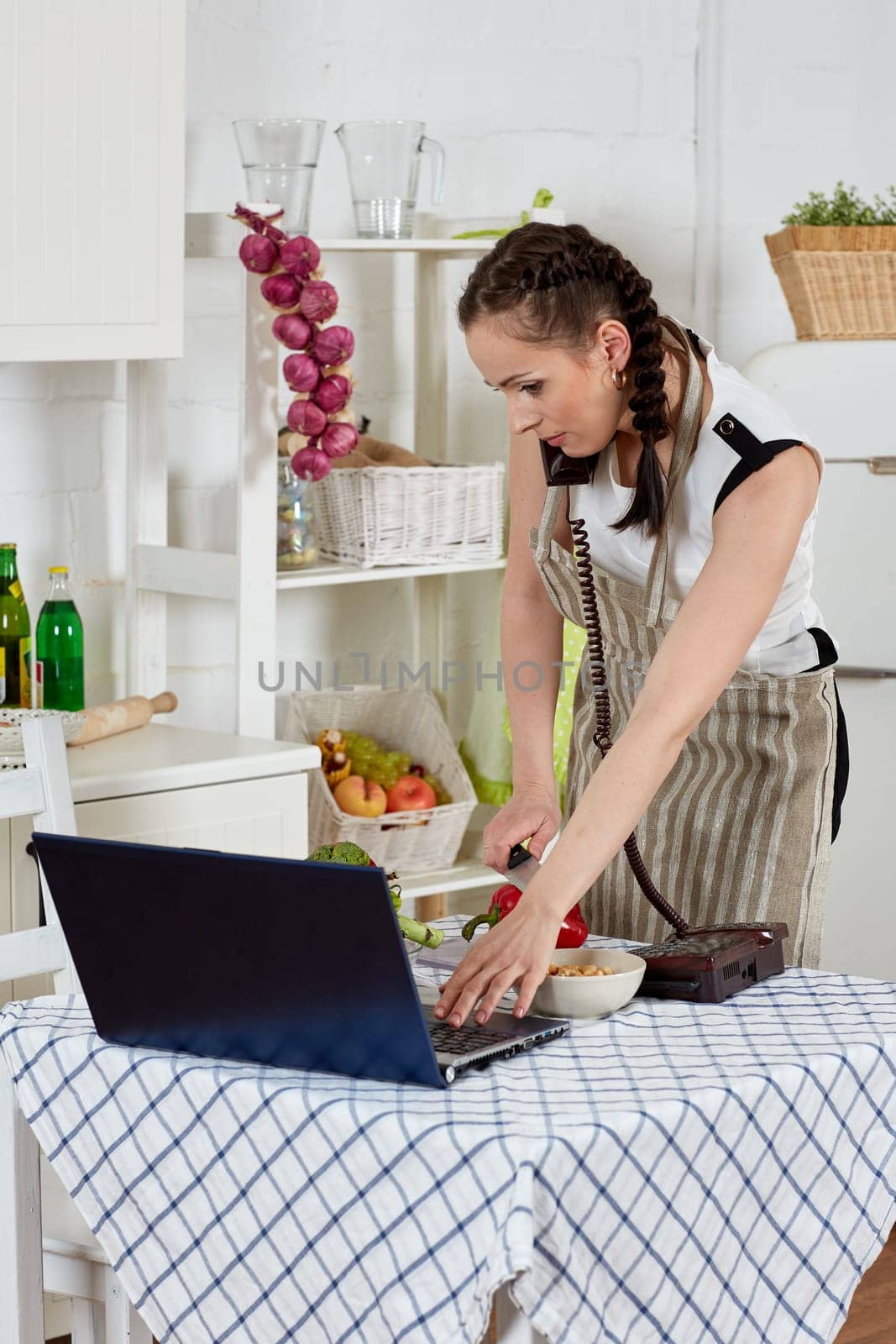 Woman in an apron with notebook and phone cooks in the kitchen. Isolation period, quarantine, social distancing. Remote education or remote work