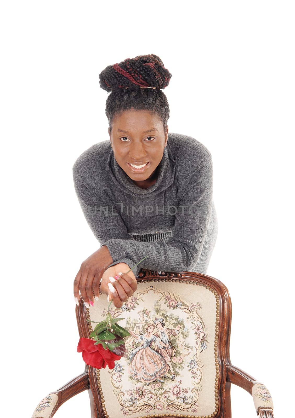 A beautiful young African American woman standing in a gray dress .behind an armchair holding a red rose, isolated for white background.