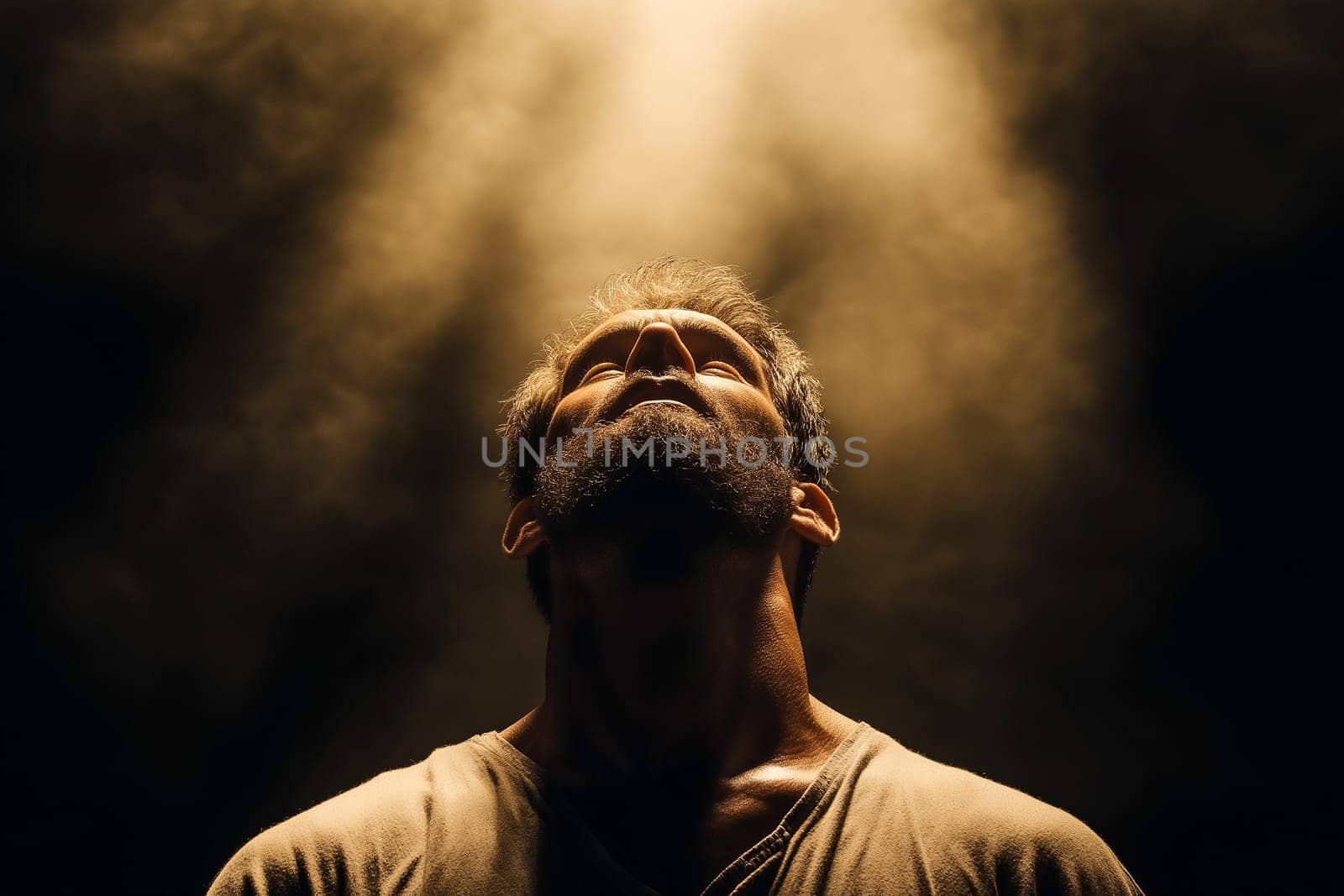 A man, head tilted upward, looks towards a light source. The soft light highlights his face, suggesting a moment of contemplation or prayer.