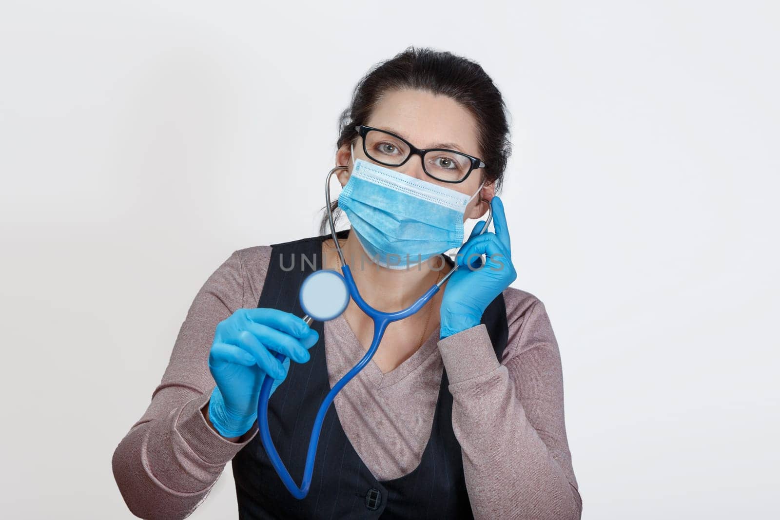 A woman in a mask and gloves with a phonendoscope in her hands with an anxious and attentive look. Self-isolation and self-control.