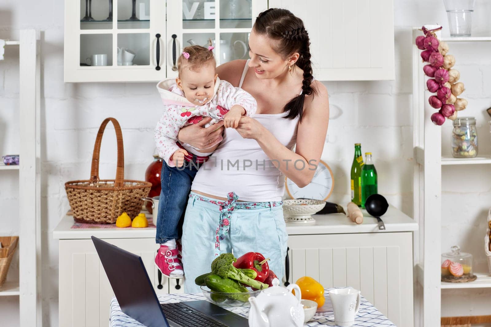 Young mother feeds little daughter  in the home kitchen. Happy family.