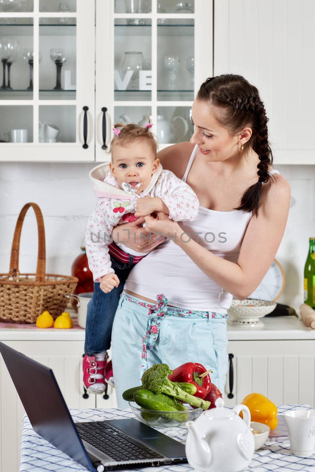 Young mother feeds little daughter  in the home kitchen. Happy family.