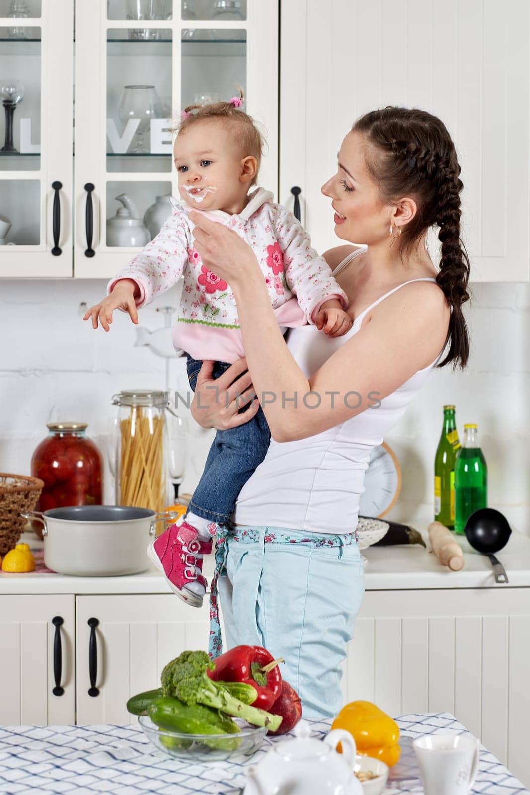 Young mother feeds little daughter  in the home kitchen. Happy family.