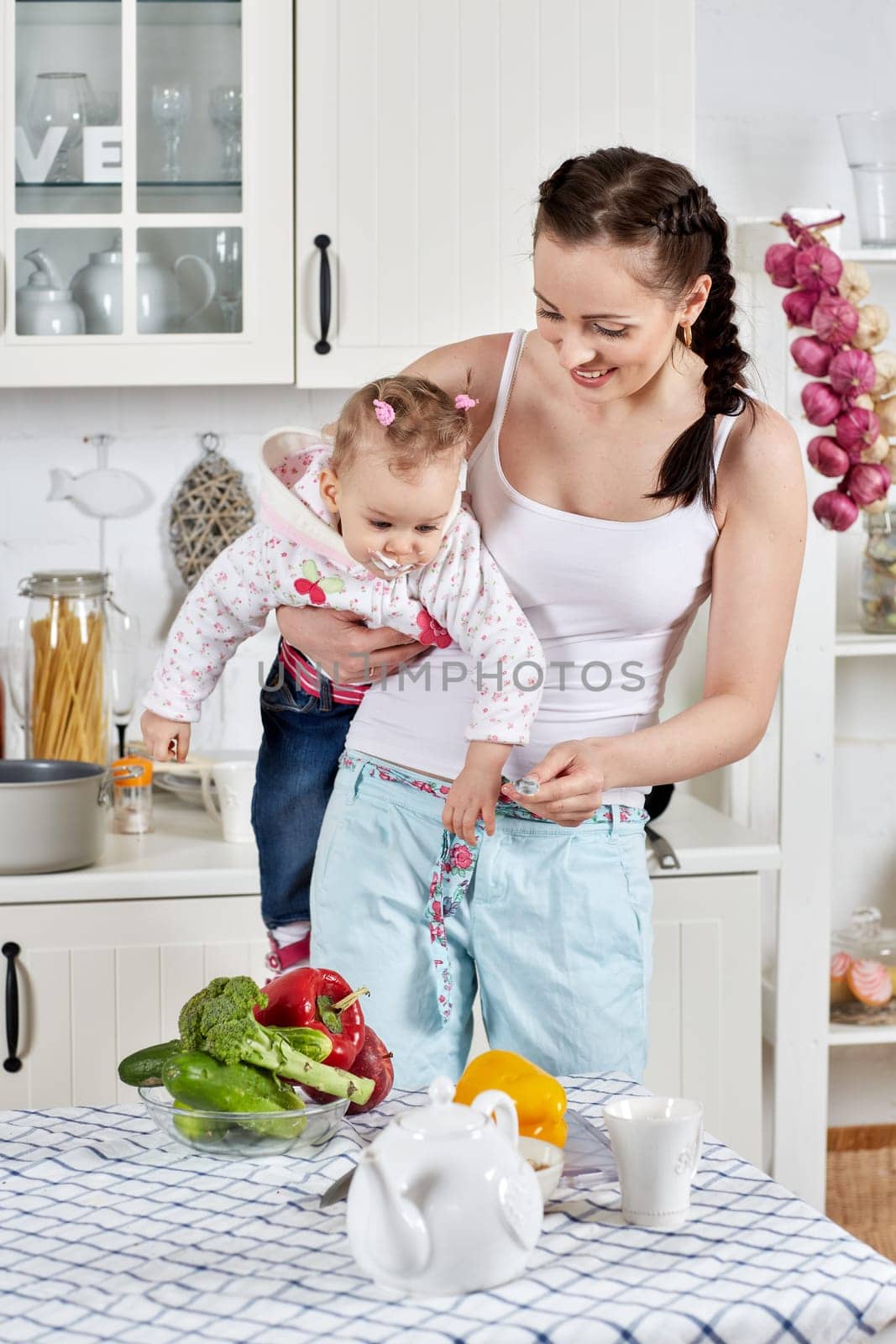Young mother feeds little daughter  in the home kitchen. Happy family.