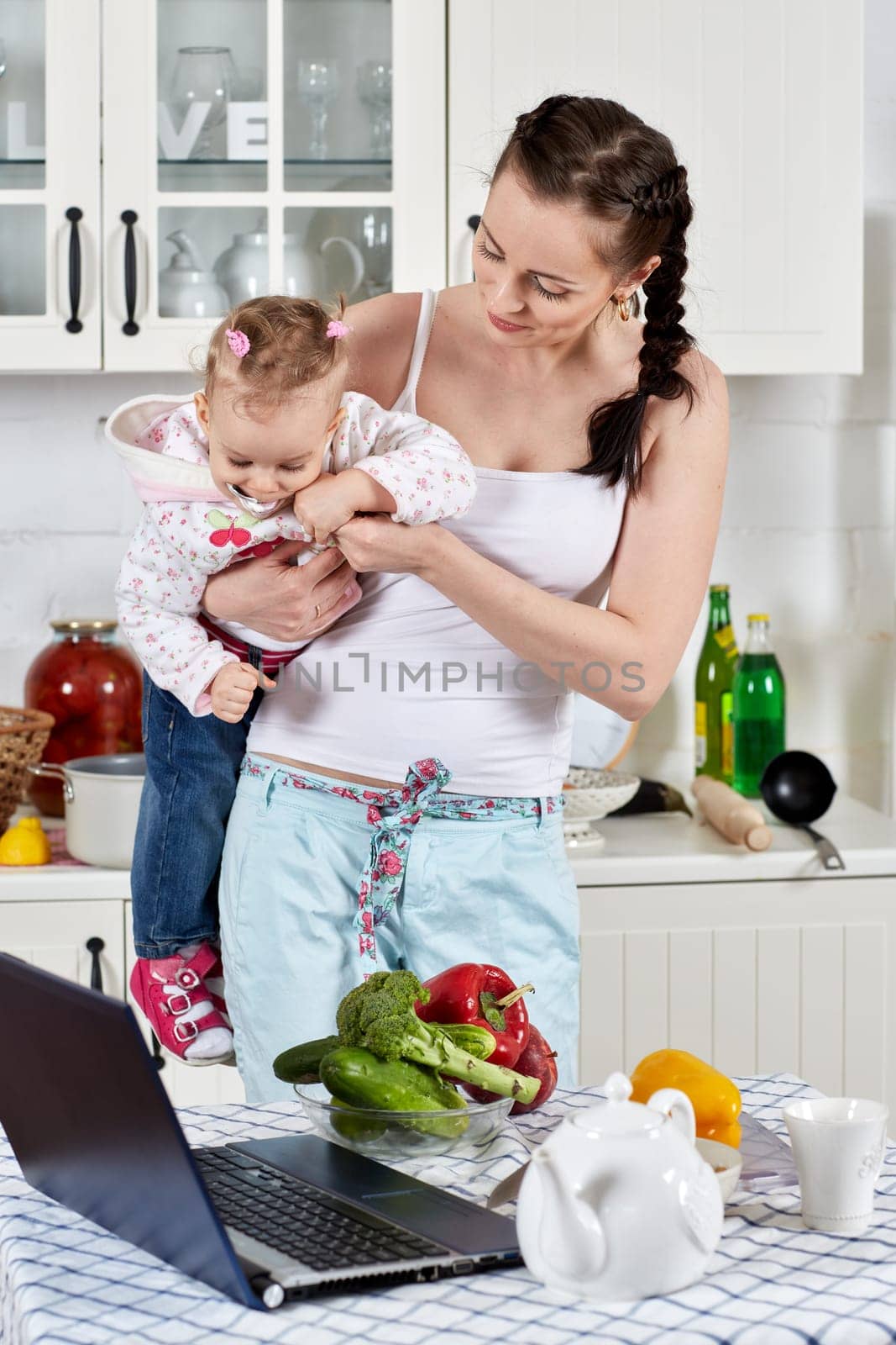Young mother feeds little daughter  in the home kitchen. Happy family.