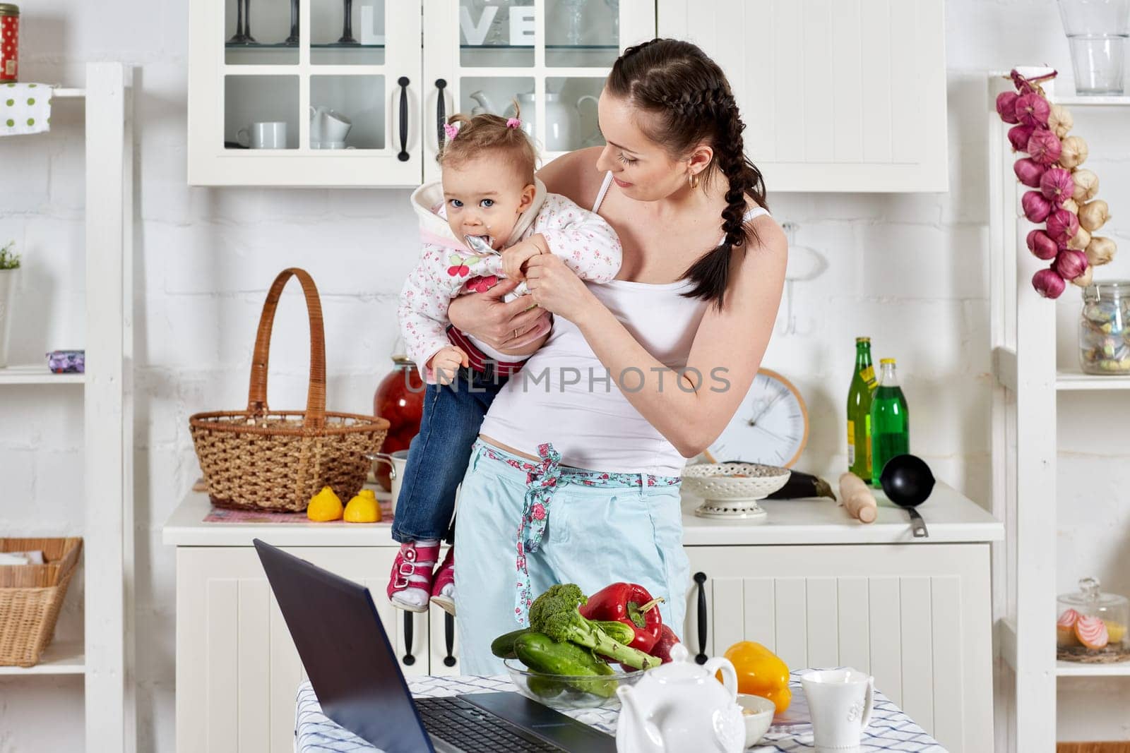 Young mother feeds little daughter  in the home kitchen. Happy family.
