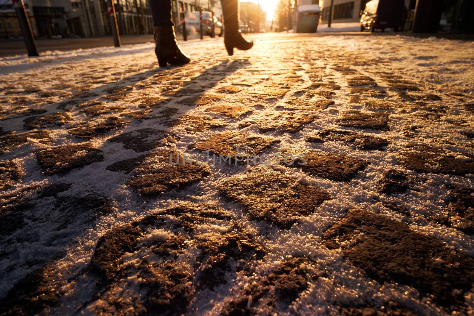 Pavement with cobblestones in winter snow and female legs
