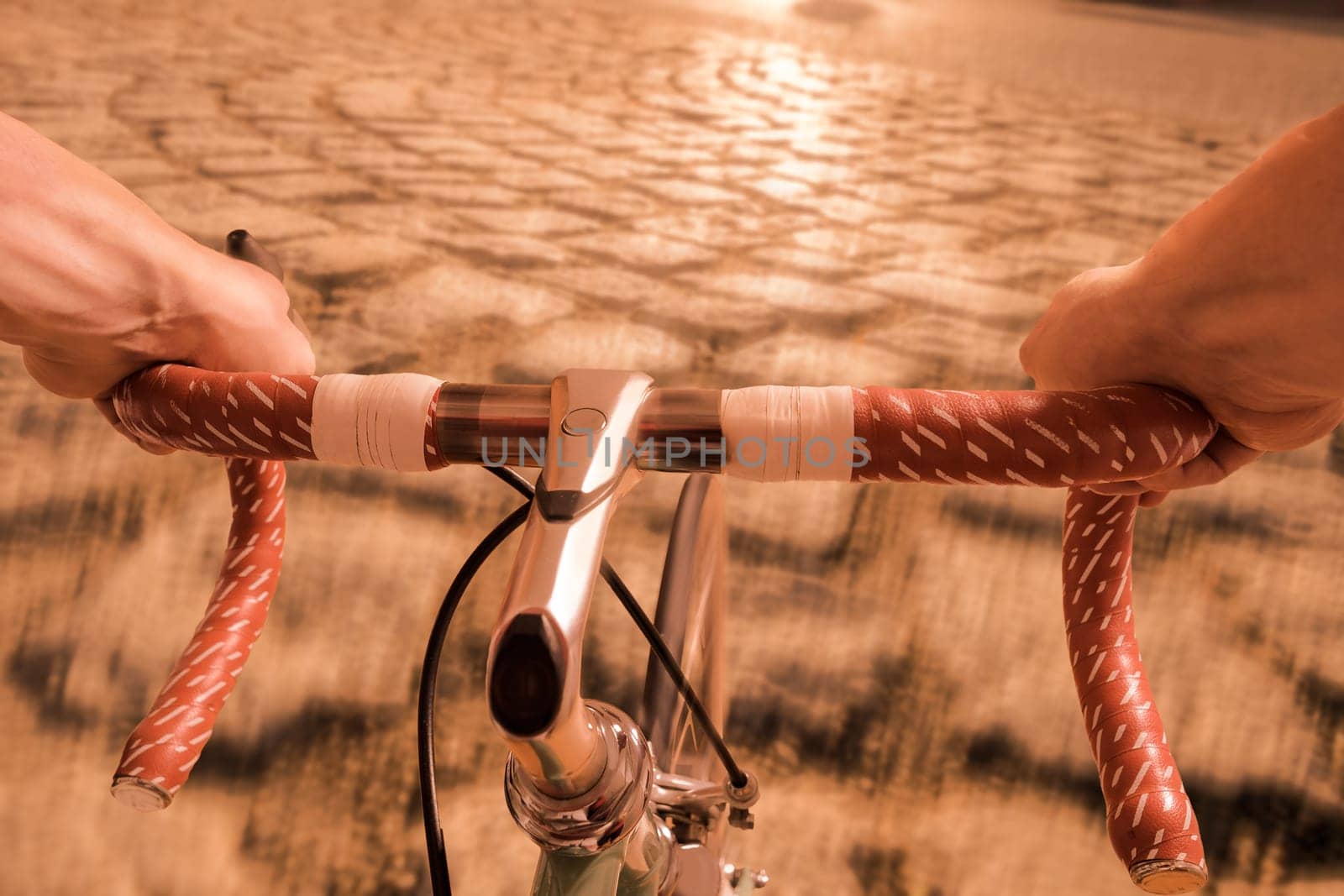Male hands at a handlebar of a bicycle and cobblestones on road