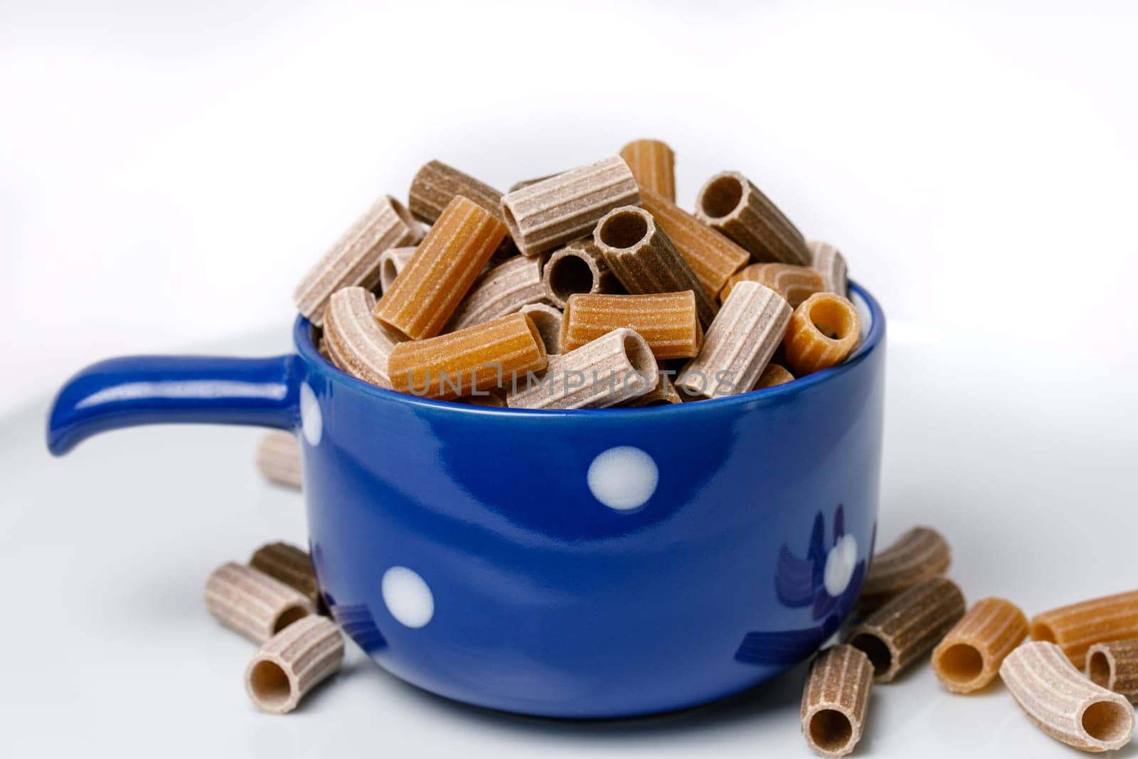 Three-colored pasta in a blue ceramic cup on a white background