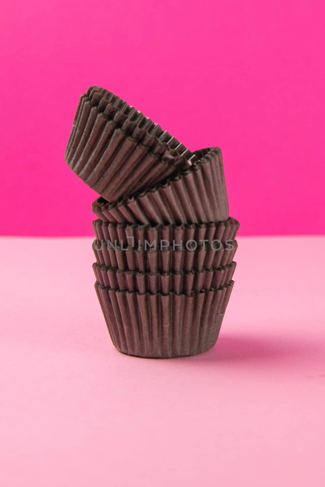 Pinc background with brown paper forms for muffins. Close-up.