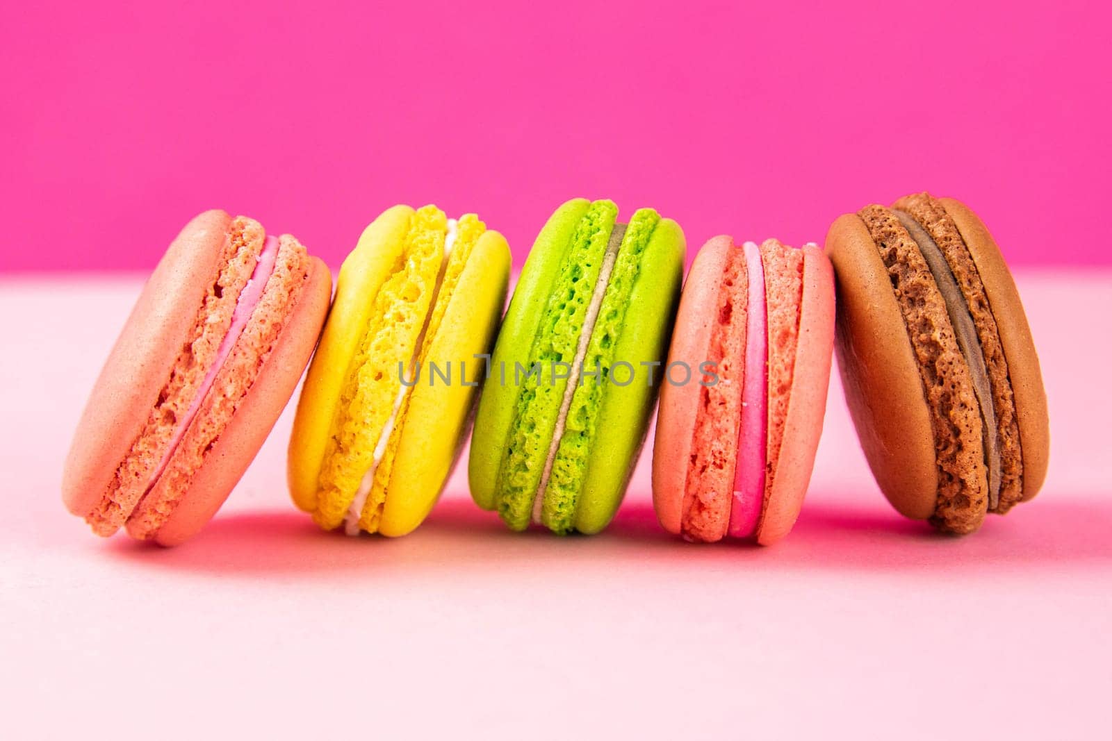 Colorful macaroons stand in a row against a pink background. Close-up