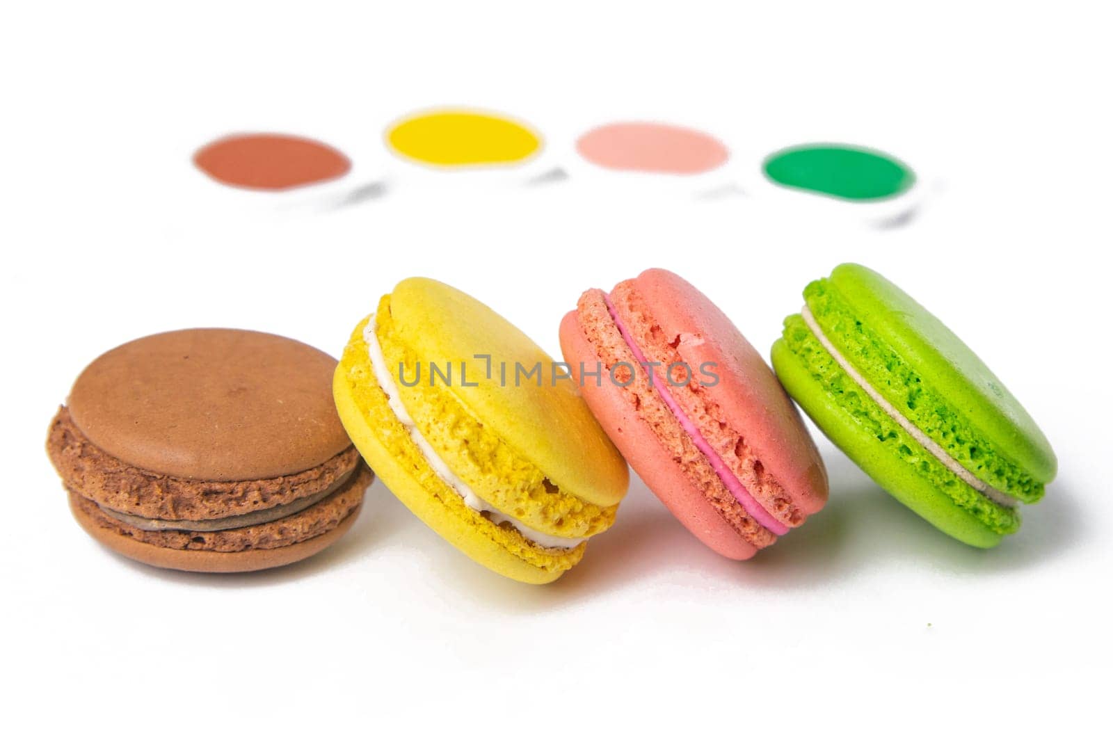 Makarons on a white background are next to the colors of macaroons and brushes for drawing. Top views with clear space.