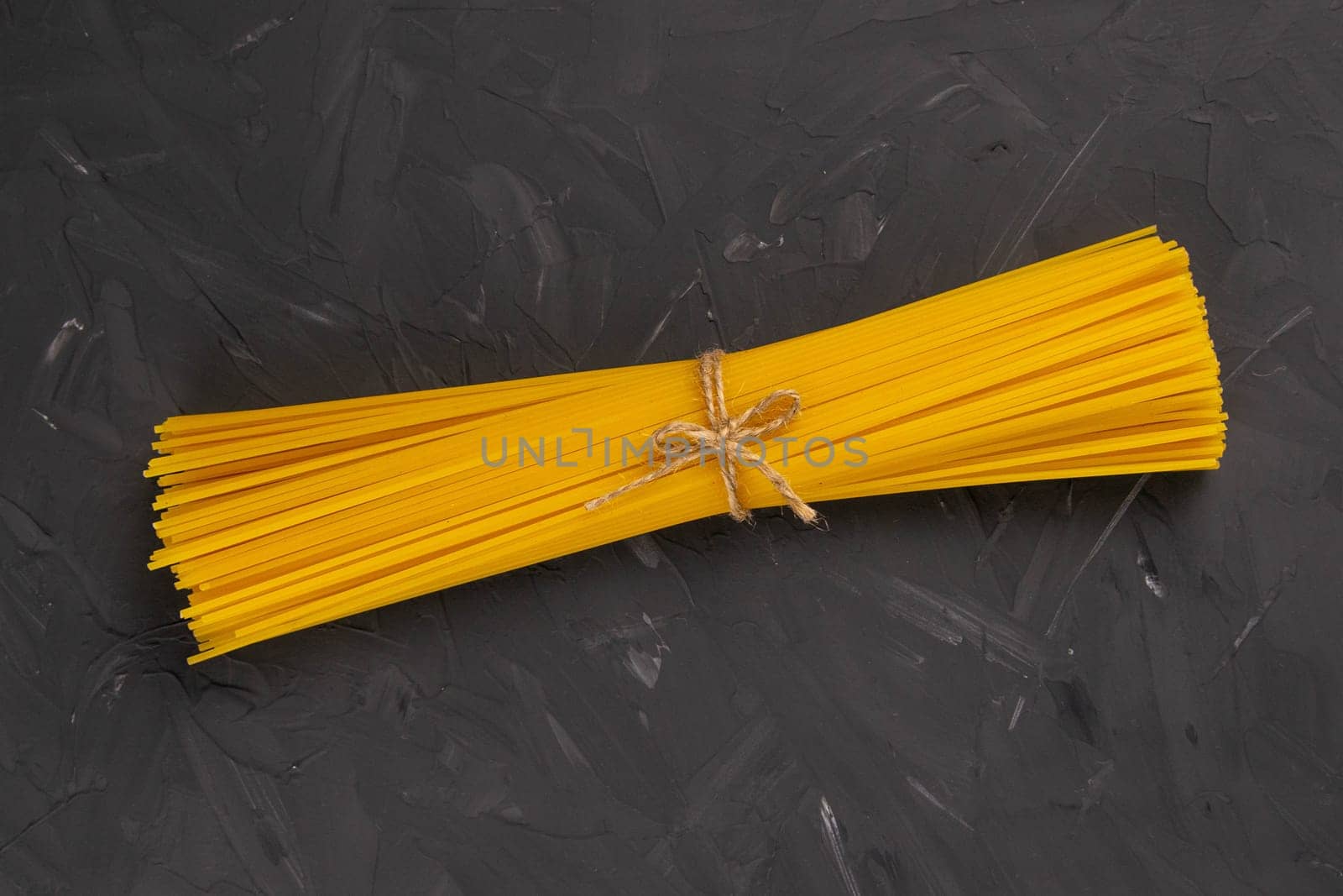 Yellow long spaghetti bound by a bagve on a dark background. Top views.